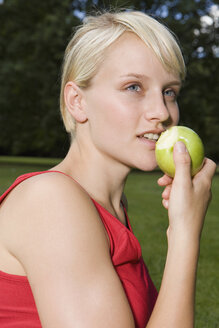 Deutschland, Berlin, Junge Frau im Park isst einen Apfel, Porträt - SKF00136