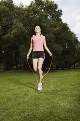 Germany, Berlin, Young woman in park jumping rope - SKF00132