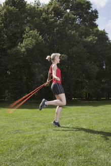 Germany, Berlin, Young woman jumping rope in park - SKF00131