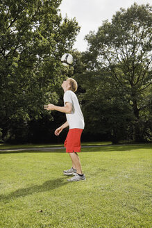 Deutschland, Berlin, Junger Mann auf Rasen mit Fußball spielend - SKF00130