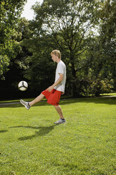 Deutschland, Berlin, Junger Mann auf Rasen mit Fußball spielend - SKF00129