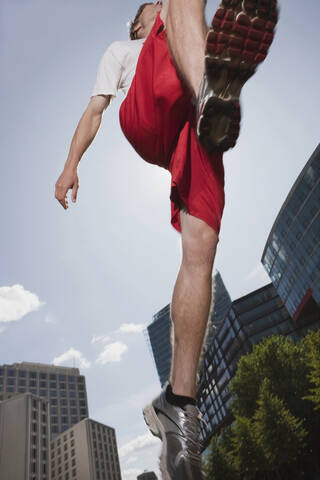 Deutschland, Berlin, Junger Mann springt in die Luft, flacher Blickwinkel, lizenzfreies Stockfoto