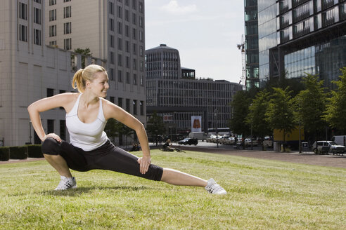 Germany, Berlin, Young woman doing stretching exercise on lawn - SKF00100