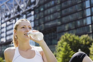 Deutschland, Berlin, Junge Frau trinkt Wasser aus Flasche, Gebäude im Hintergrund, Porträt - SKF00086