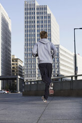 Deutschland, Berlin, Junger Mann beim Joggen, Wolkenkratzer im Hintergrund - SKF00056