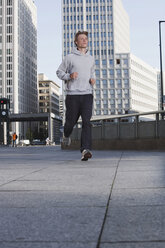 Deutschland, Berlin, Junger Mann beim Joggen, Wolkenkratzer im Hintergrund - SKF00054