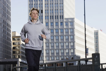 Deutschland, Berlin, Junger Mann beim Joggen, Wolkenkratzer im Hintergrund - SKF00052