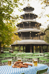 Deutschland, Bayern, Englischer Garten, Bierkrüge und Brezeln auf dem Tisch, Chinesischer Turm im Hintergrund - WESTF14086