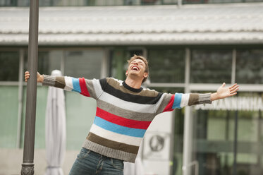 Germany, Bavaria, Munich, Man standing next to lamp post, arm outstretched, eyes closed, looking up, portrait - WESTF14059