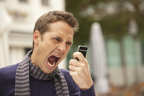 Germany, Bavaria, Munich, Man holding mobile phone, screaming, portrait - WESTF14054