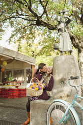 Germany, Bavaria, Munich, Viktualienmarkt, Couple by fountain holding basket with flowers, portrait - WESTF14043