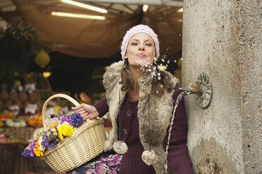 Germany, Bavaria, Munich, Viktualienmarkt, Woman sitting by fountain, splashing water - WESTF14040