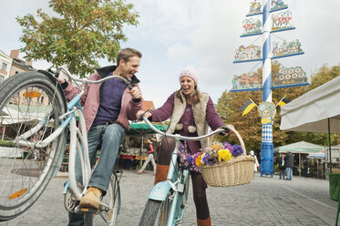 Germany, Bavaria, Munich, Viktualienmarkt, Couple with bicycles, laughing, portrait - WESTF14036