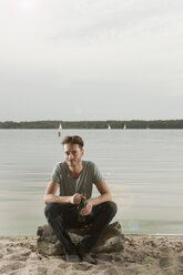 Deutschland, Berlin, Junger Mann sitzt auf einem Felsen am See, Porträt - WESTF13969