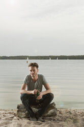 Germany, Berlin, Young man sitting on rock near lake, portrait - WESTF13969