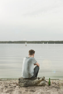 Germany, Berlin, Young man sitting on rock near lake, rear view - WESTF13968