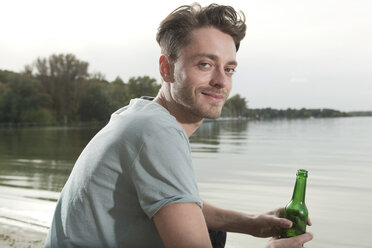 Germany, Berlin, Lake Wannsee, Young man holding bottle, smiling, portrait - WESTF13967