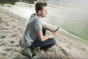 Deutschland, Berlin, Junger Mann sitzt auf einem Felsen am See, Porträt - WESTF13966