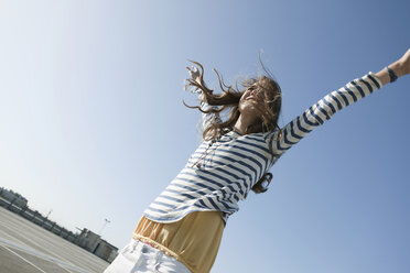 Germany, Berlin, Young woman on parking level, raising arms, smiling, portrait - WESTF13923