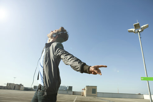 Germany, Berlin, Young man on deserted parking level wearing headphones listening to music - WESTF13915