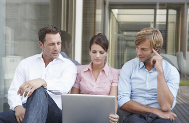 Deutschland, Köln, Drei Geschäftsleute, die nebeneinander sitzen und einen Laptop benutzen - JOF00094