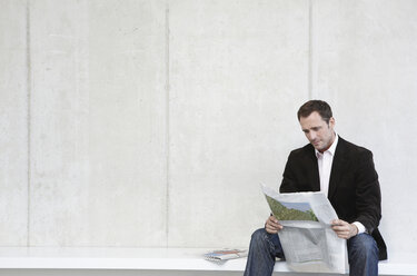 Germany, Cologne, Businessman sitting on bench reading newspaper, portrait - JOF00060