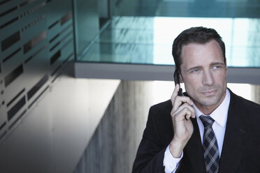 Germany, Cologne, Businessman in staircase using mobile phone, portrait, close-up - JOF00050