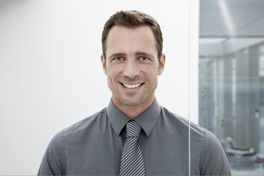 Germany, Cologne, Businessman standing next glass door, smiling, portrait, close-up - JOF00020