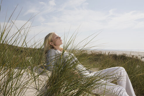 Germany, Schleswig Holstein, Amrum, Woman relaxing in dunes, eyes closed - RBF00173