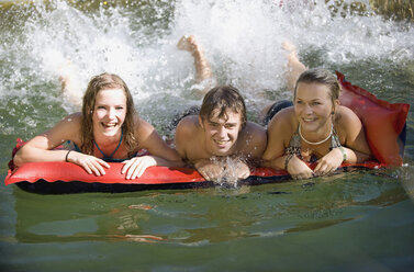 Österreich, Salzburger Land, Jugendliche (14-15) auf Luftmatratze spritzen Wasser, lachend, Porträt - WWF01125