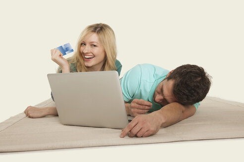 Pärchen mit Laptop liegend, Mann schlafend und Frau hält Kreditkarte - WESTF14596
