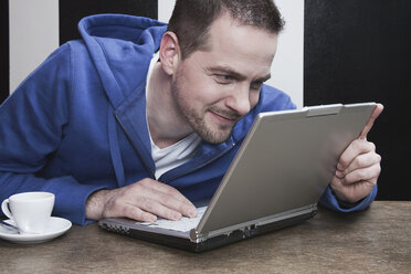 Mann starrt auf Laptop, lächelnd - WESTF14408