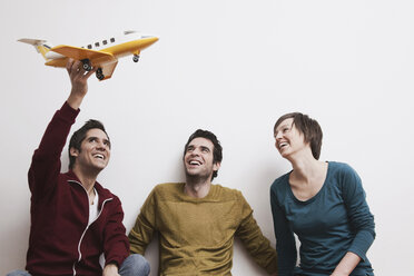 Men and women playing with toy aeroplane, smiling. - WESTF14382