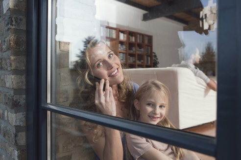 Germany, Cologne, Mother and daughter (6-7) sitting by window, mother using mobile phone, portrait - WESTF14353