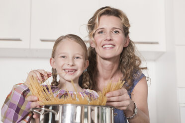 Germany, Cologne, Mother and daughter (6-7) cooking pasta, smiling, portrait - WESTF14346