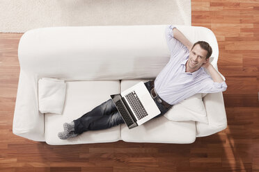 Germany, Cologne, Man with laptop relaxing on sofa, elevated view - WESTF14305