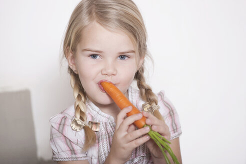 Germany, Cologne, Girl (4-5) with braids eating a carrot, portrait, close-up - WESTF14288