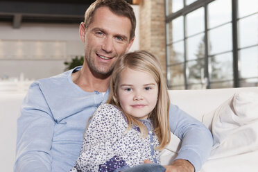 Germany, Cologne, Father and daughter (6-7) sitting on sofa, smiling, portrait - WESTF14254