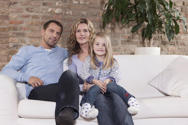 Germany, Cologne, Family sitting on sofa in living room, smiling, portrait - WESTF14242