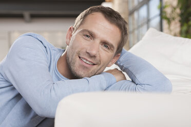 Germany, Cologne, Man sitting by sofa, smiling, portrait - WESTF14235