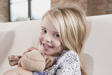 Germany, Cologne, Girl (4-5) with a stuffed toy, sitting on sofa - WESTF14234
