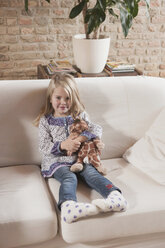 Germany, Cologne, Girl (4-5) with a stuffed toy, sitting on sofa - WESTF14230