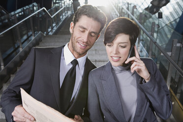 Germany, Bavaria, Munich, Two business people on staircase at underground station, business woman using mobile phone, portrait - WESTF14139