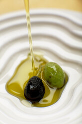 Olive oil poured over olive, elevated view, close-up - SCF00371