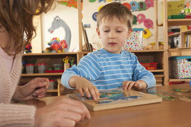 Germany, Female nursery teacher and boy (4-5) doing jigsaw puzzle, portrait - RNF00218