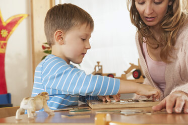 Germany, Female nursery teacher and boy (4-5) doing jigsaw puzzle, portrait - RNF00215