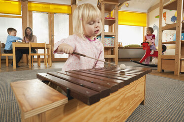 Deutschland, Mädchen (3-4) spielt Xylophon, Kindergärtnerin mit Kindern im Hintergrund, Portrait - RNF00211