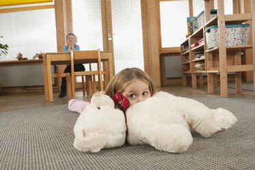 Deutschland, Mädchen (3-4) im Kinderzimmer auf dem Boden liegend, Junge (4-5) im Hintergrund am Tisch sitzend, Hände am Kinn, Porträt - RNF00207