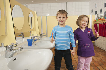Deutschland, Junge (4-5) und Mädchen (3-4) stehen Hand in Hand auf der Toilette und halten Zahnbürsten, lächelnd, Porträt - RNF00196