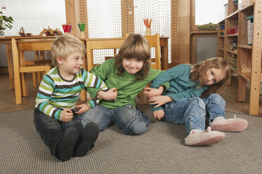 Deutschland, Drei Kinder im Kinderzimmer auf dem Boden sitzend, lächelnd, Porträt - RNF00166